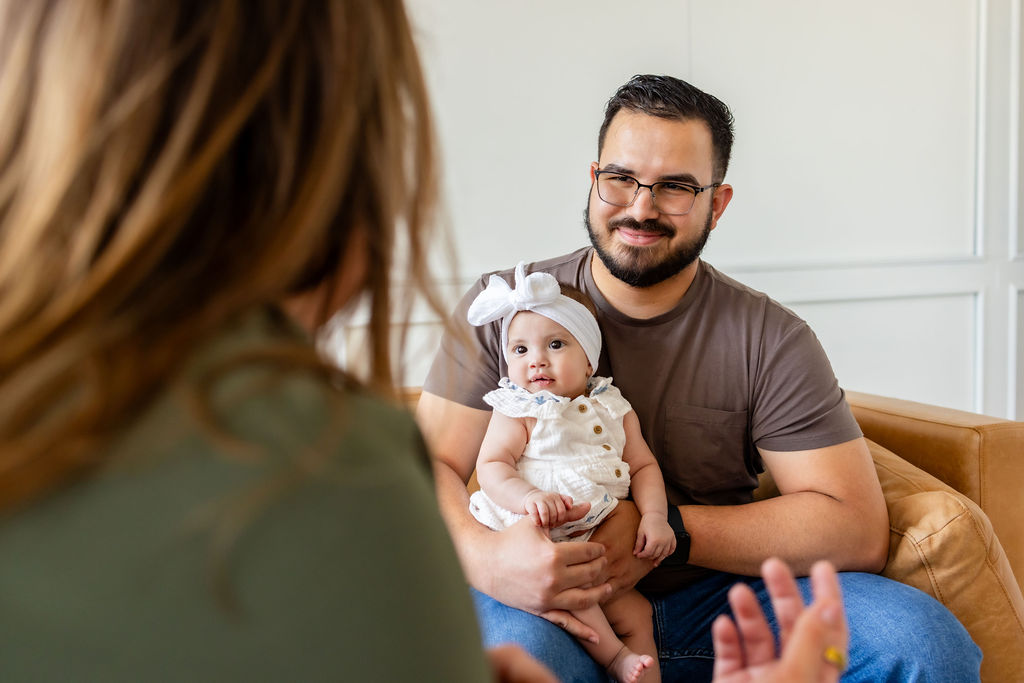 A father holding an infant while talking with a clinician