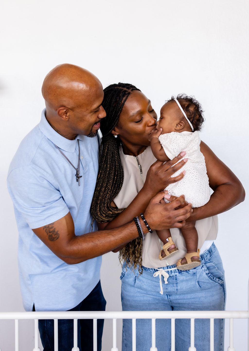 Parents smiling and leaning toward their infant beside a crib