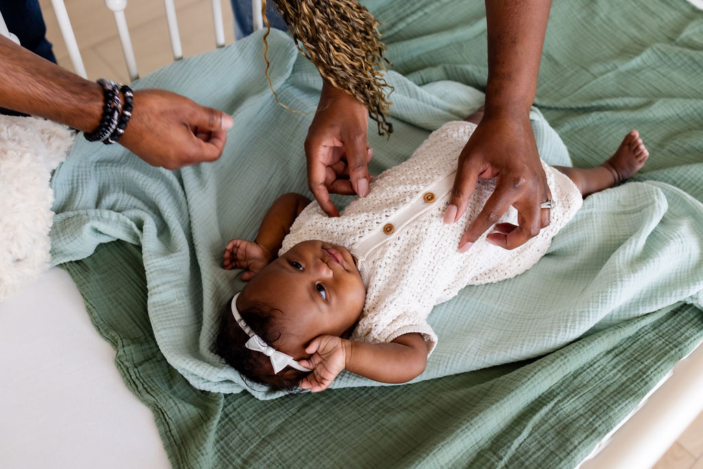 A caregiver resting her hands on an awake infant's tummy and legs