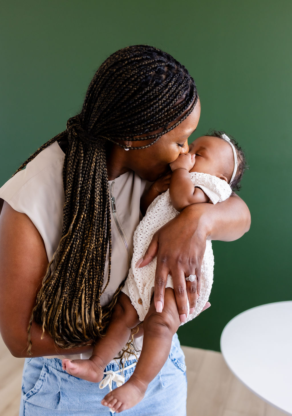A caregiver cuddling her infant against a green background