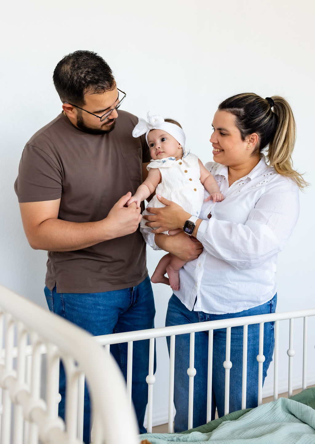 Parents holding their infant beside a white crib