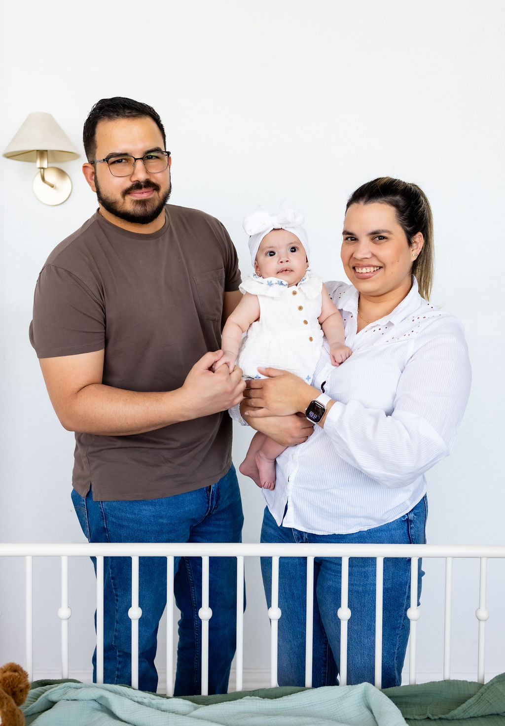 Parents holding their infant beside a white crib